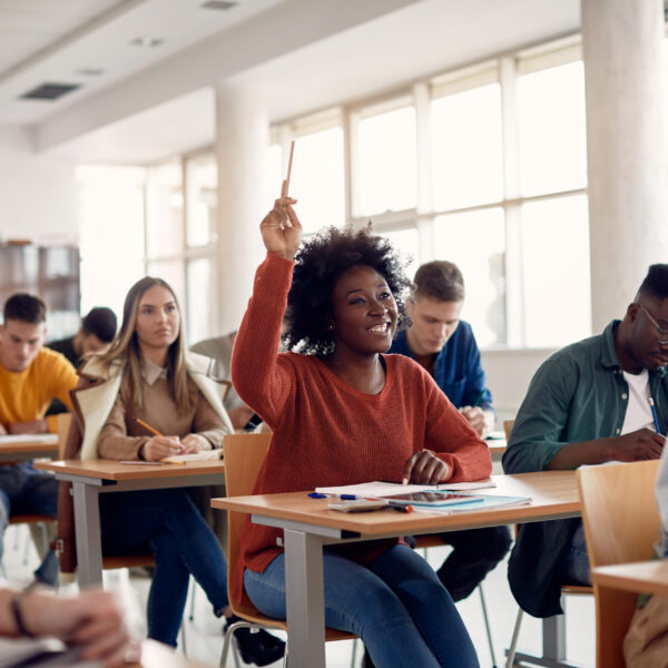 Happy African American student raising her hand to ask a question during lecture in the classroom.