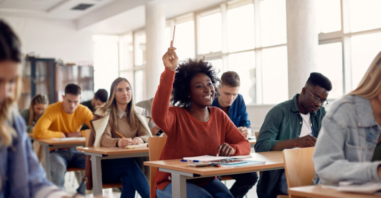 Happy African American student raising her hand to ask a question during lecture in the classroom.