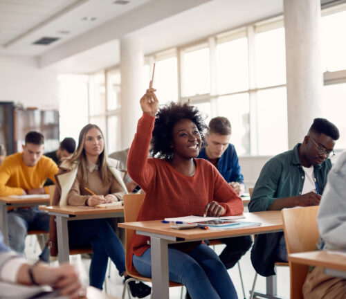 Happy African American student raising her hand to ask a question during lecture in the classroom.